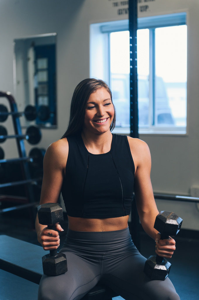 beautiful athletic girl smiling and holding weights about to enjoy a hemp protein shake